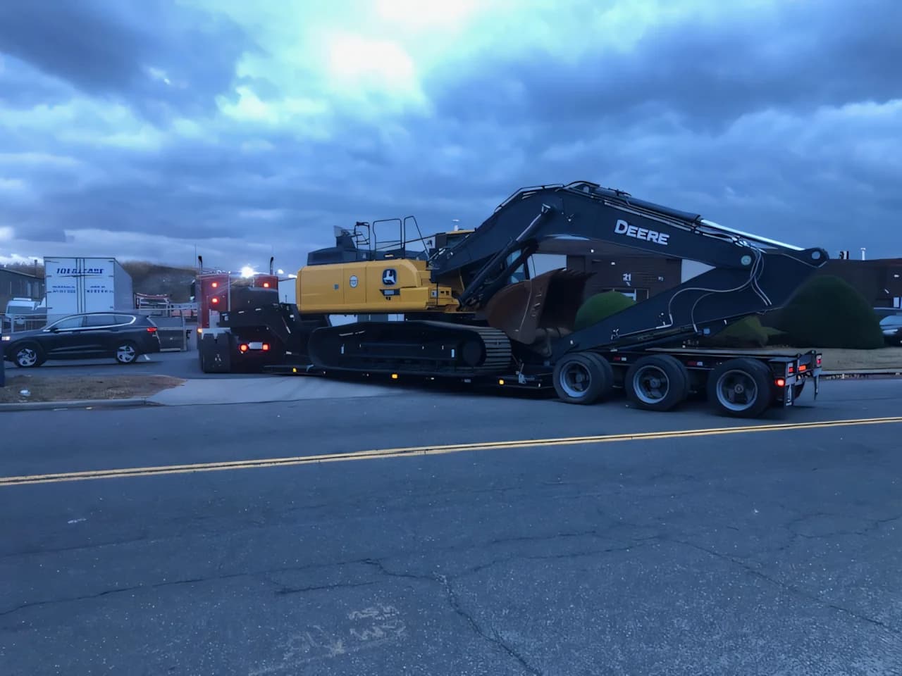 John Deere excavator secured on a Campbell Logistics flatbed trailer at dusk